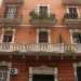 Foto 9. Ripercorriamo per un breve tratto via Manzoni per arrivare in via Crisanzio. Scopriamo qui un brillante palazzo arancione, il cui balcone al primo piano mostra una bellissima balaustra in pietra e le lesene delle persiane decorate